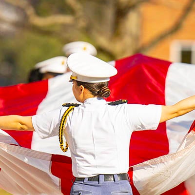 A cadet in a white uniform holds out a large red and white fabric banner