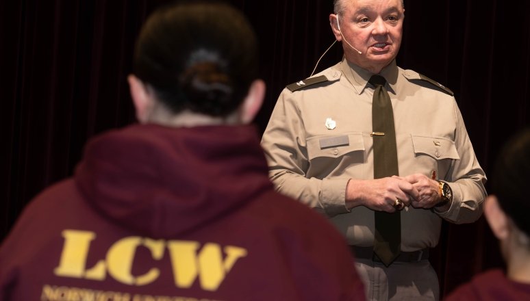 Person in uniform speaks to people wearing maroon hoodies labeled LCW Norwich University.