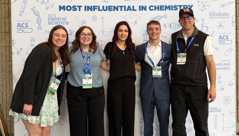 Five people pose with conference badges in front of an ACS Chemistry for Life backdrop.