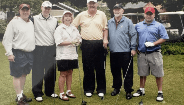 Six golfers pose with clubs on a grassy course near golf carts.